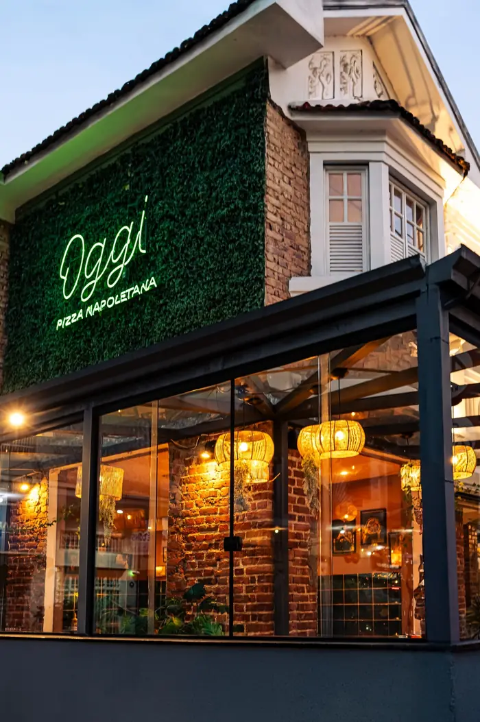 Fachada da Oggi Tijuca com parede verde e letreiro em neon