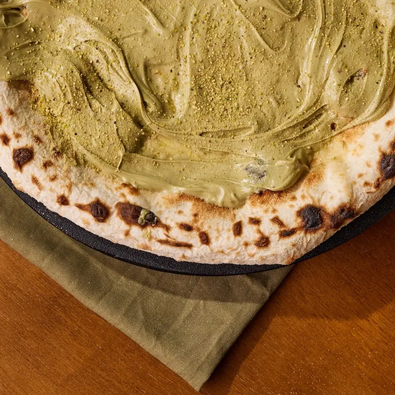 Borda de pizza napoletana com as manchas tostadas típicas, coberta com creme de pistache